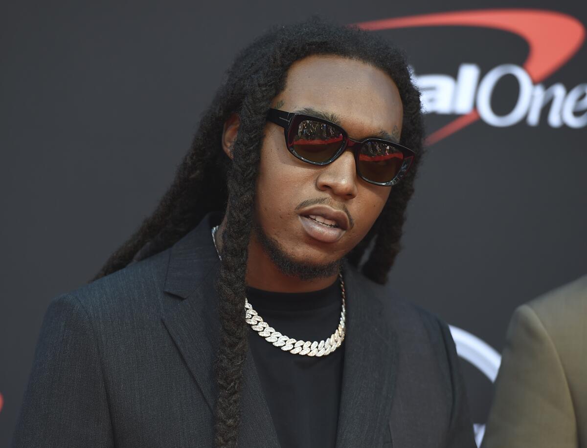 Rapper Takeoff wears black sunglasses as he poses for photos wearing a black shirt, black blazer and a gold necklace.  