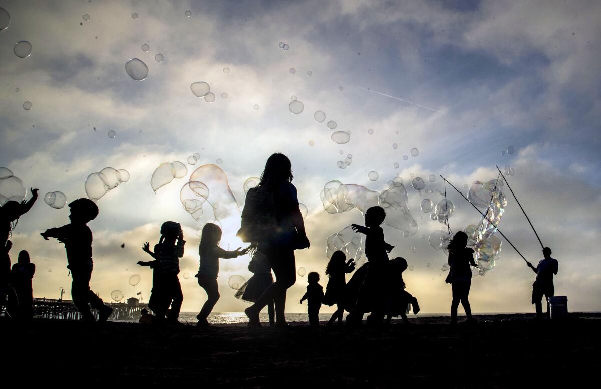 In silhouette, kids play around the bubble man known as Frenchie near San Clemente Pier.