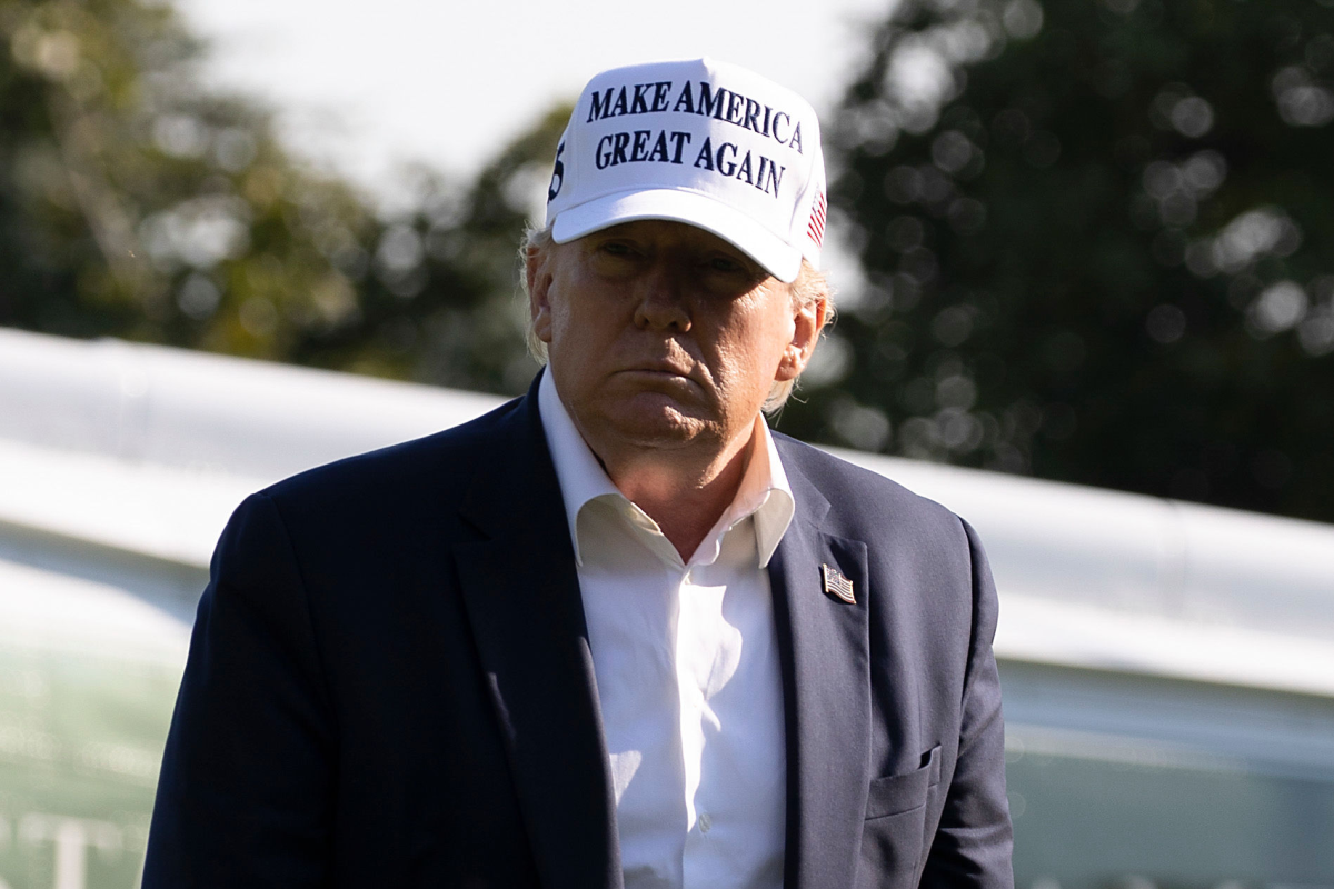 President Trump seen outside from the chest up, wearing a navy blazer and white "Make America great again" ballcap.