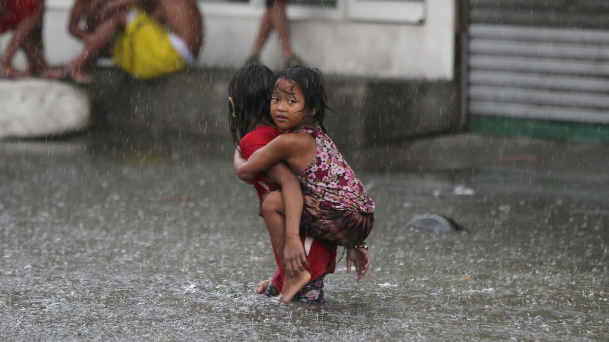 A Filipino girl is carried along a flooded road east of Manila during a record-breaking monsoon season in 2016. A new analysis says extreme weather events will become more common around the world as the global average temperature rises.