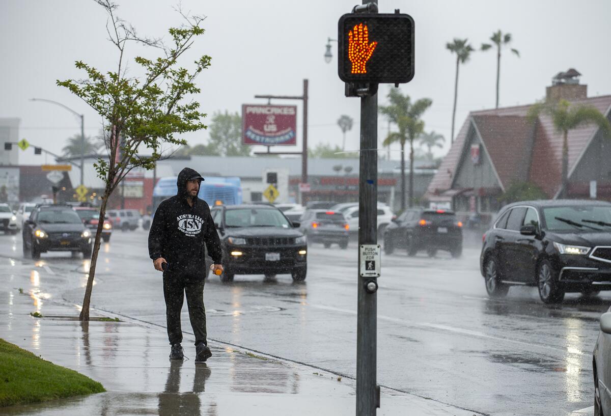 A man walks along E 17th Street in Newport Beach during a downpour on Monday.