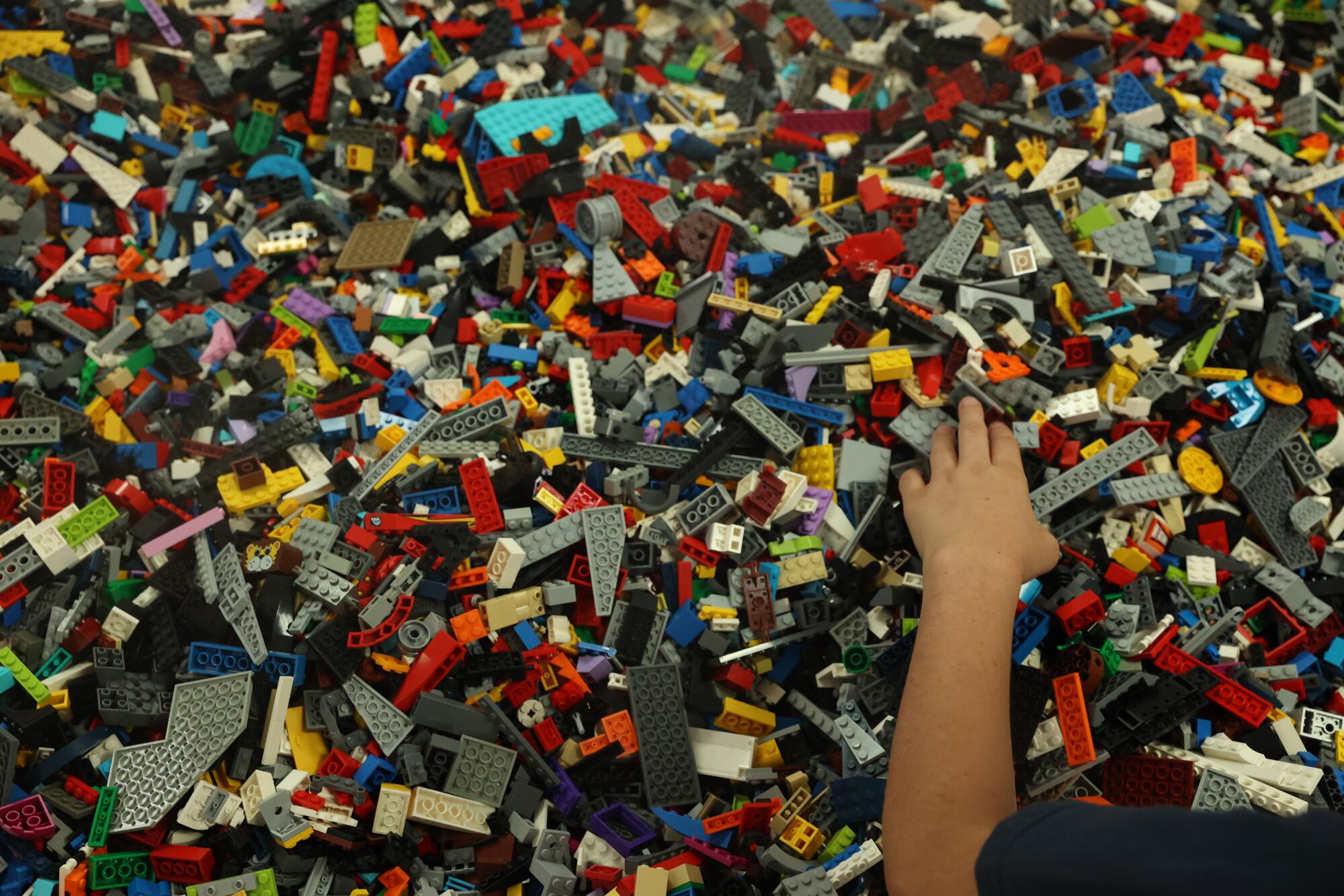 A child's arm sorting through a pile of loose Lego pieces