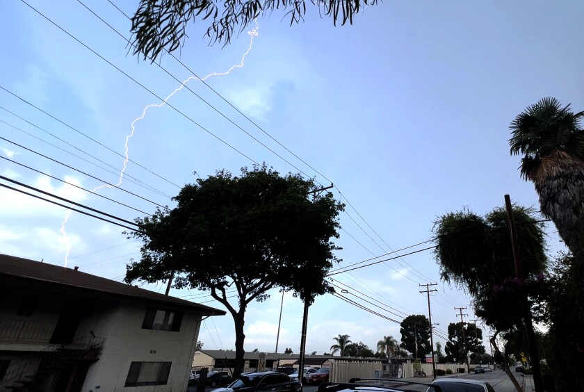 A lightning bolt is seen in a blue sky above a neighborhood street