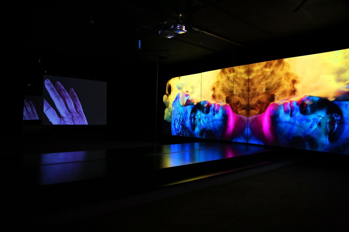 Pictured: (Reflected in mirrors) "Aftermath," right (2015) -- 1-channel video, Color with an original score by Deru, aspect ratio 16:9. dimensions variable, 7 min 40 sec loop, Ed 2/4 ; "Ancient Hand," left, (2015) -- 1-channel video, color, silent, aspect ratio 4:3 or 16:9 dimensions variable, 6 min 44 sec loop, Ed 2/4.
