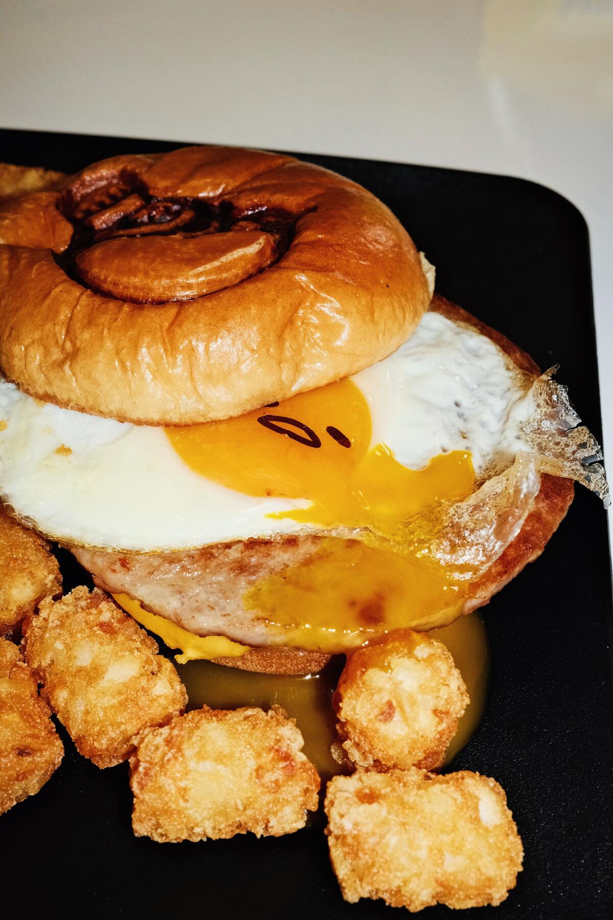A closeup of a yolk oozing on an egg-topped sausage sandwich with tots at the Gudetama Cafe in Buena Park