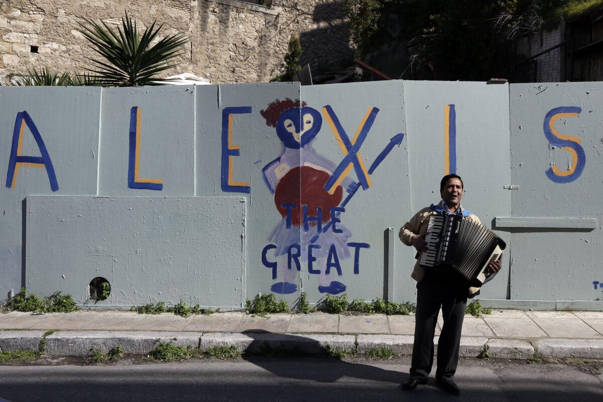 A busker performs Saturday in front of graffiti referring to new Greek Prime Minister Alexis Tsipras, who has promised to ease austerity measures that were imposed on Greece in exchange for European bailout funds.