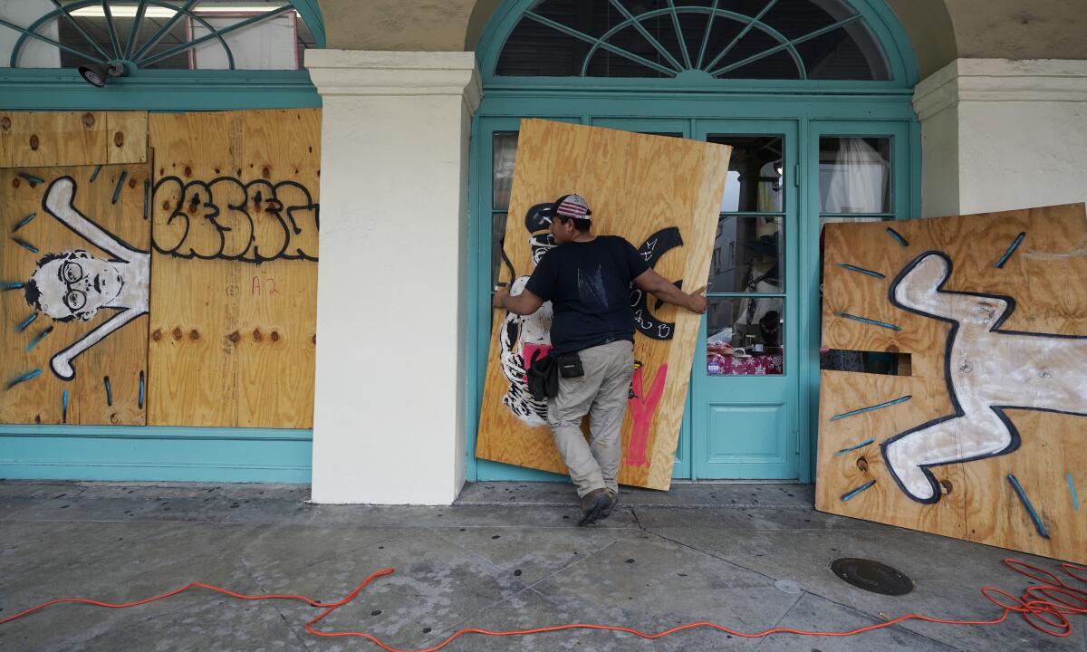 A worker attaches protective plywood to windows and doors of a business.