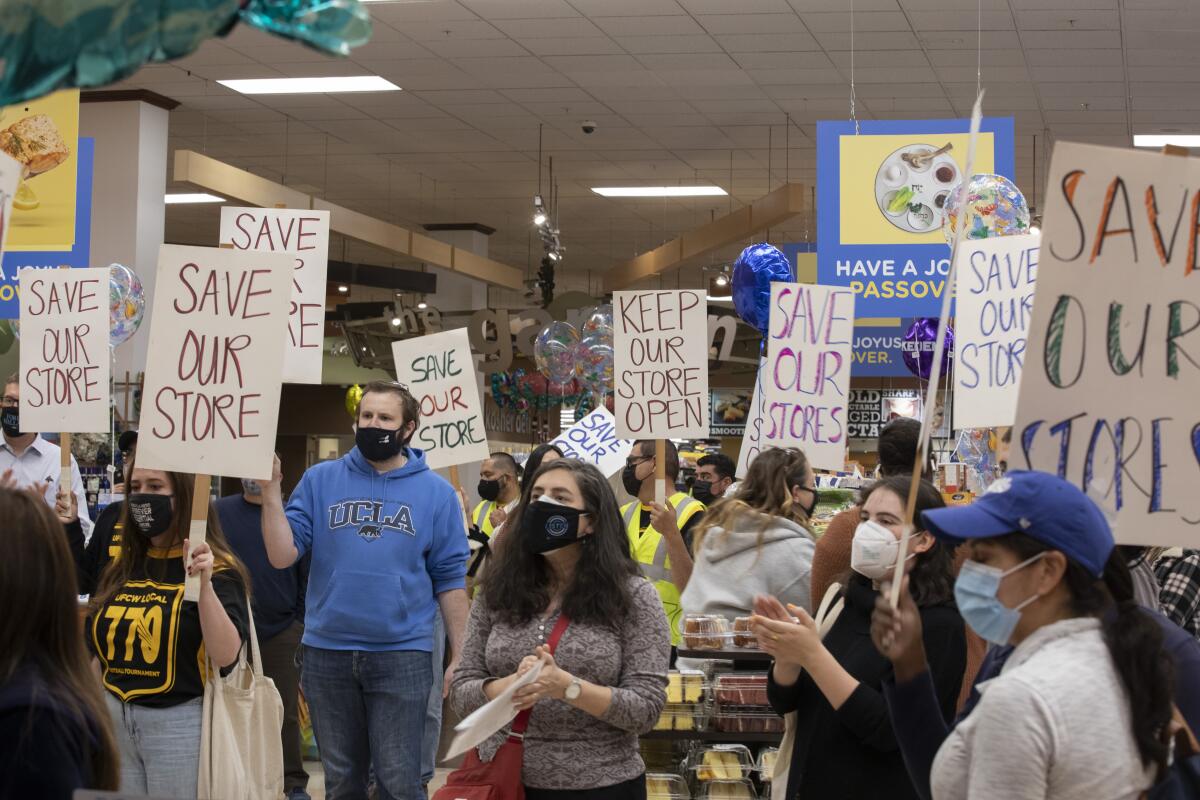 Protesters inside a supermarket with signs that say Save Our Store and Keep Our Store Open