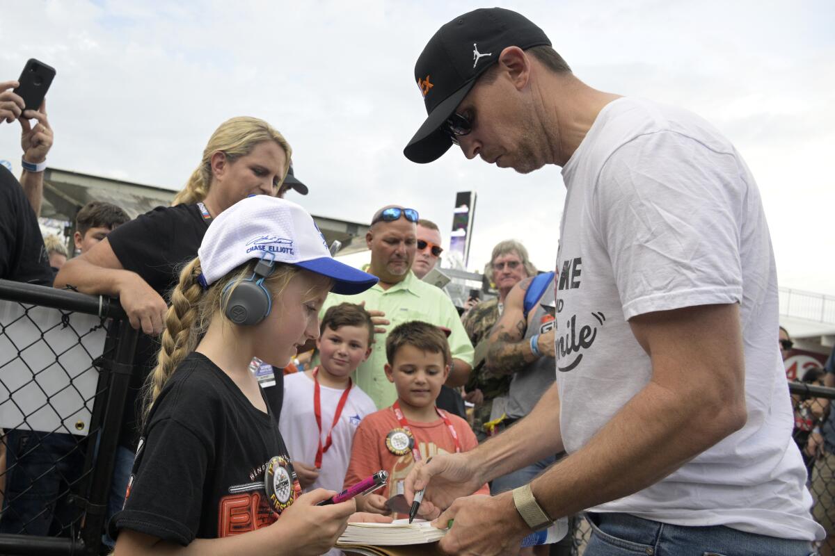 Denny Hamlin, right, gives autographs to fans before a NASCAR Cup Series auto race at Daytona International Speedway, Friday, Aug. 26, 2022, in Daytona Beach, Fla. (AP Photo/Phelan M. Ebenhack)