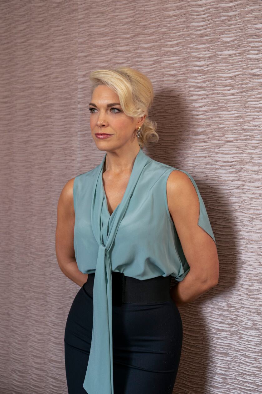 A woman in a pastel blue blouse standing against a pink wall