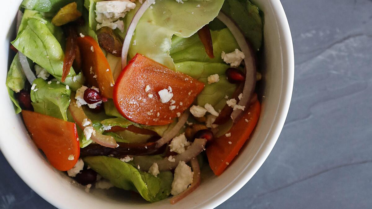 This early winter salad features sliced ​​persimmons, pomegranate seeds, and feta cheese with hot lettuce and red onions.
