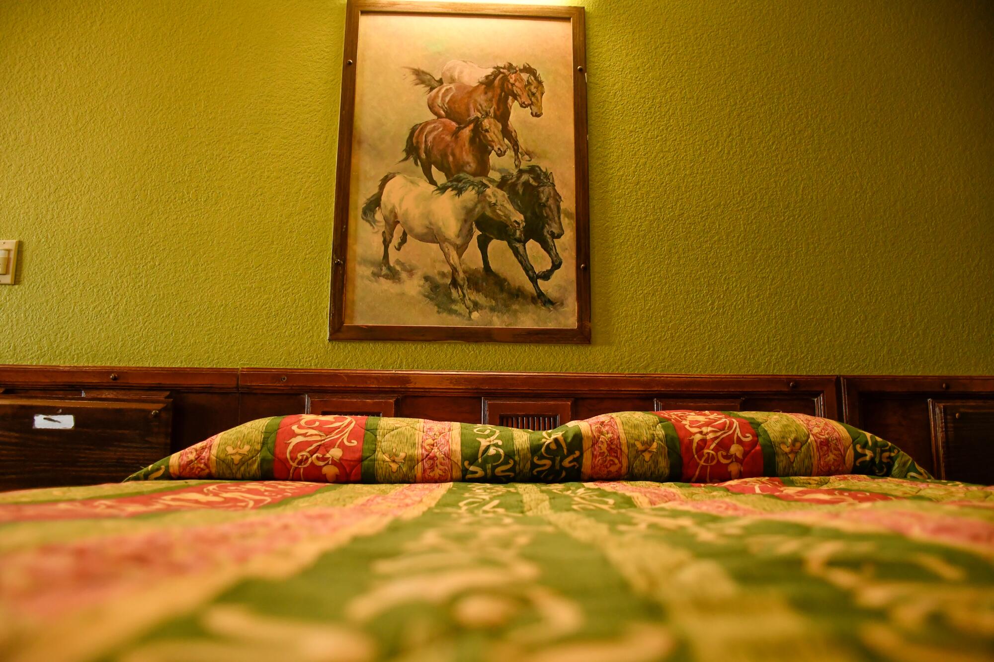 A bed with a painting of horses above it 