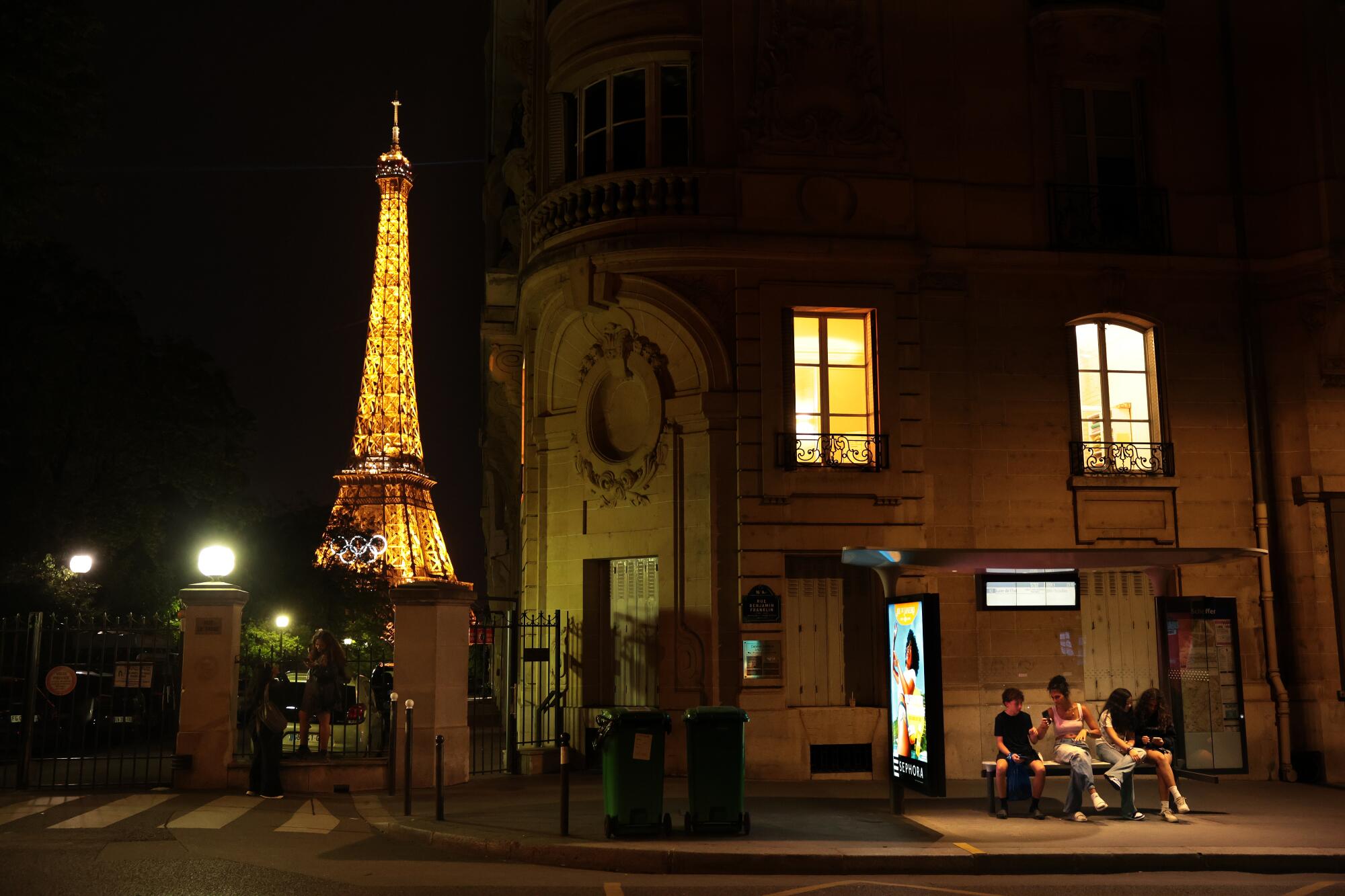 People sit at a bus stop in Paris on Tuesday night, three days before the start of the Olympic Games.