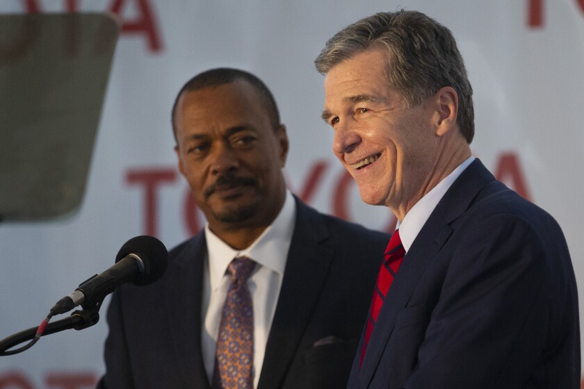 North Carolina Gov. Roy Cooper smiles as Toyota Motor Administrative Officer Chris Reynolds, left, stands with him to celebrate their new partnership during an announcement of the future site of a new Toyota battery manufacturing plant in Liberty, N.C., Monday, Dec. 6, 2021. (Kenneth Ferriera/News & Record via AP)