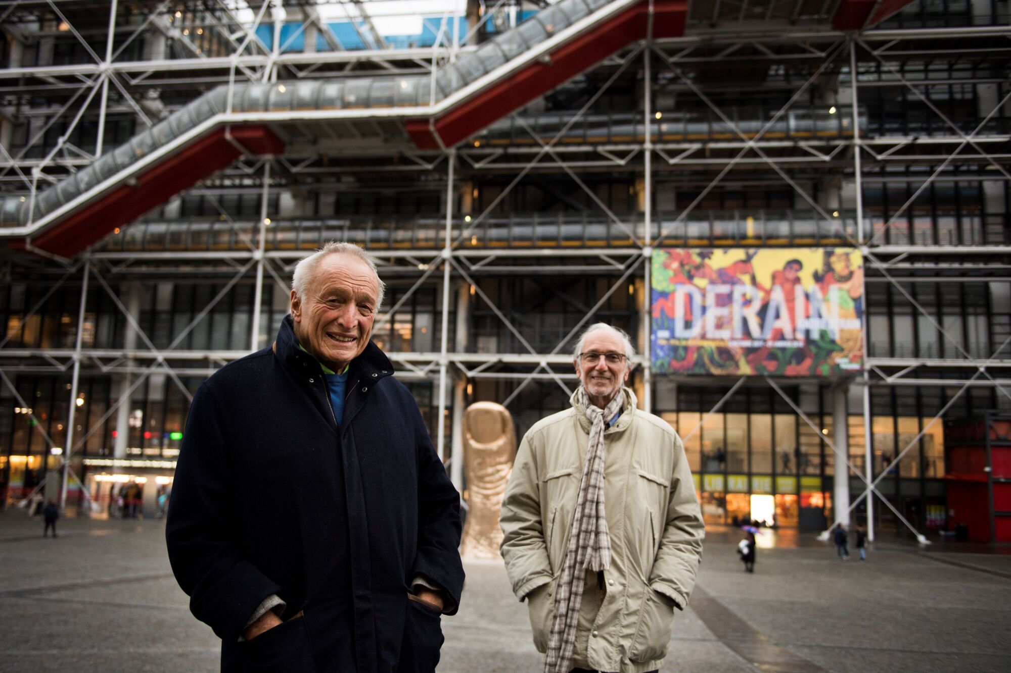 Renzo Piano and Richard Rogers smile as they stand in front of one of the machine-like escalators of the Pompidou