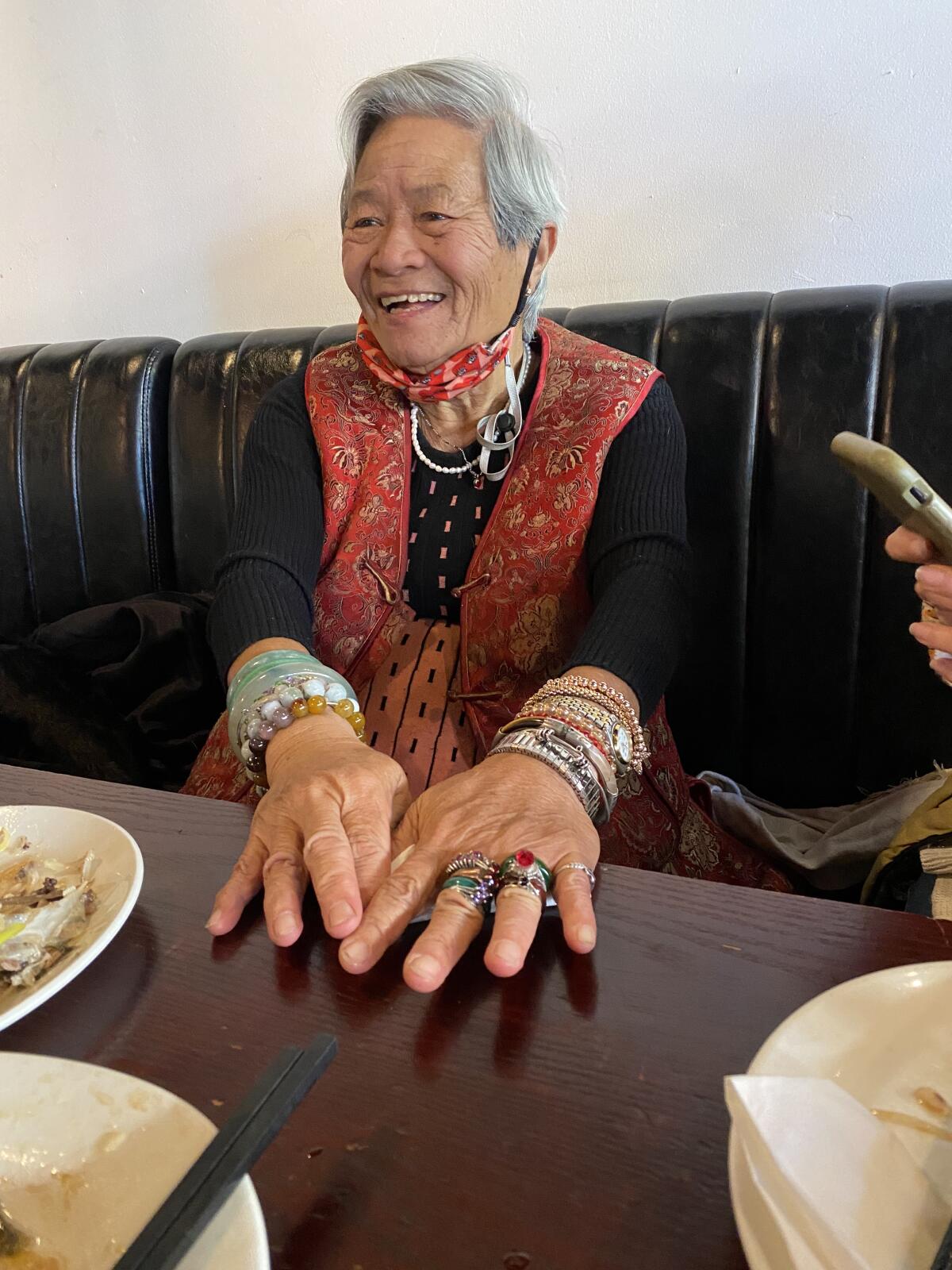 A smiling woman with multiple bracelets sits at a restaurant booth.
