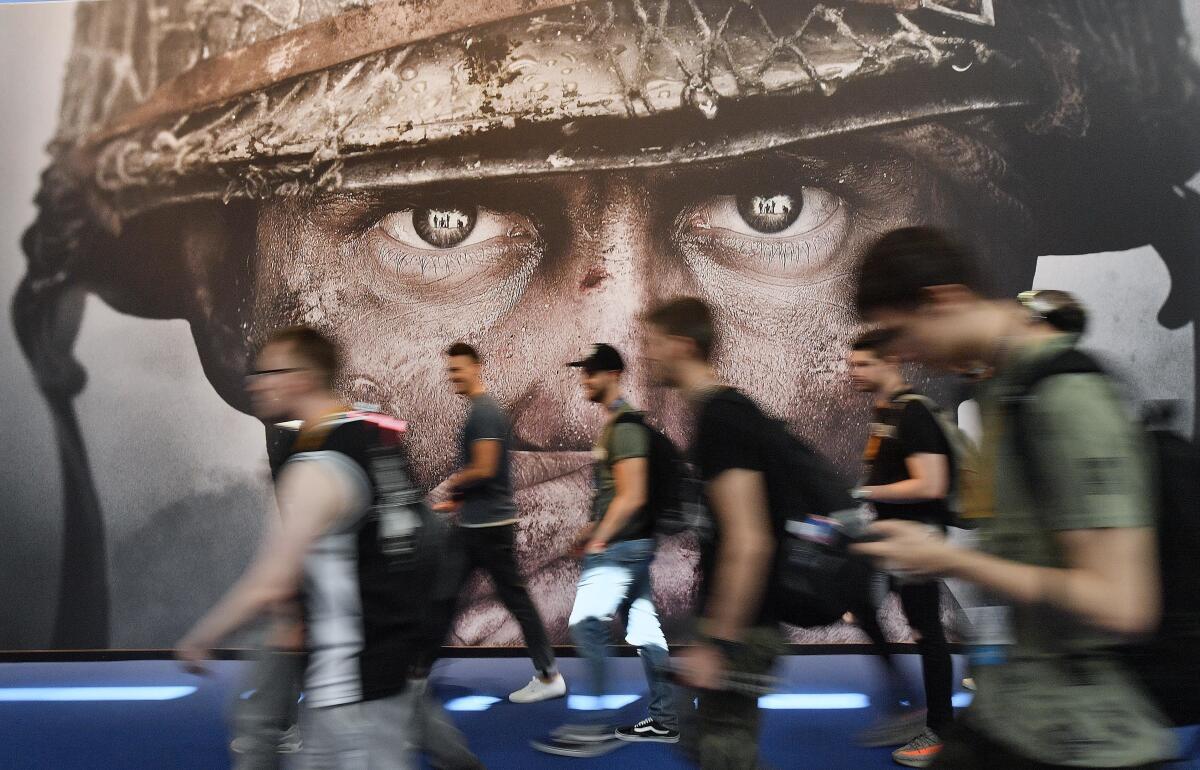 People walk in front of a giant photo of the head of a person in a helmet.