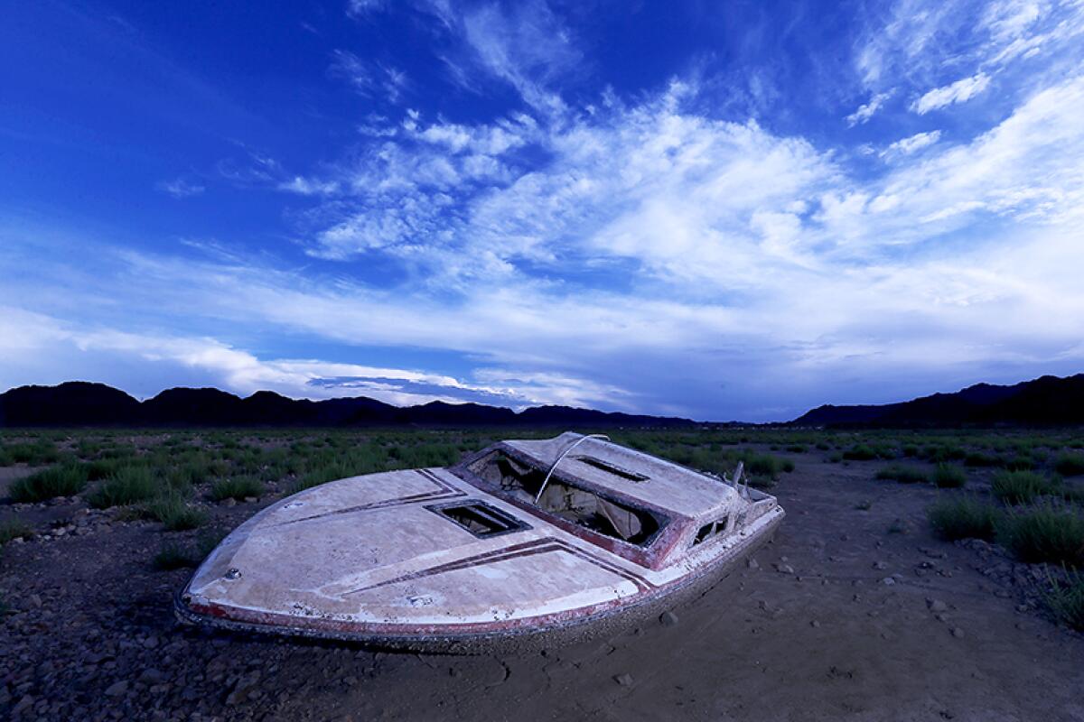 An old boat sits amid mud and dirt, with blue sky and clouds above.