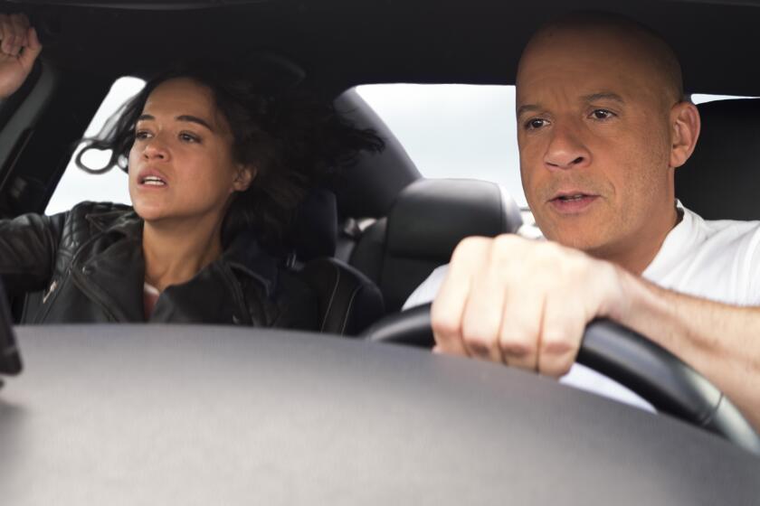 Michelle Rodriguez holds on as Vin Diesel drives a car.