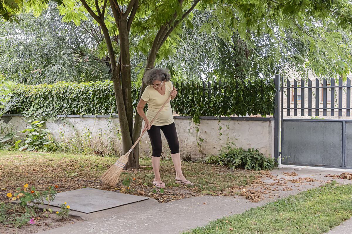 A woman uses her broom to sweep walkways and driveways.