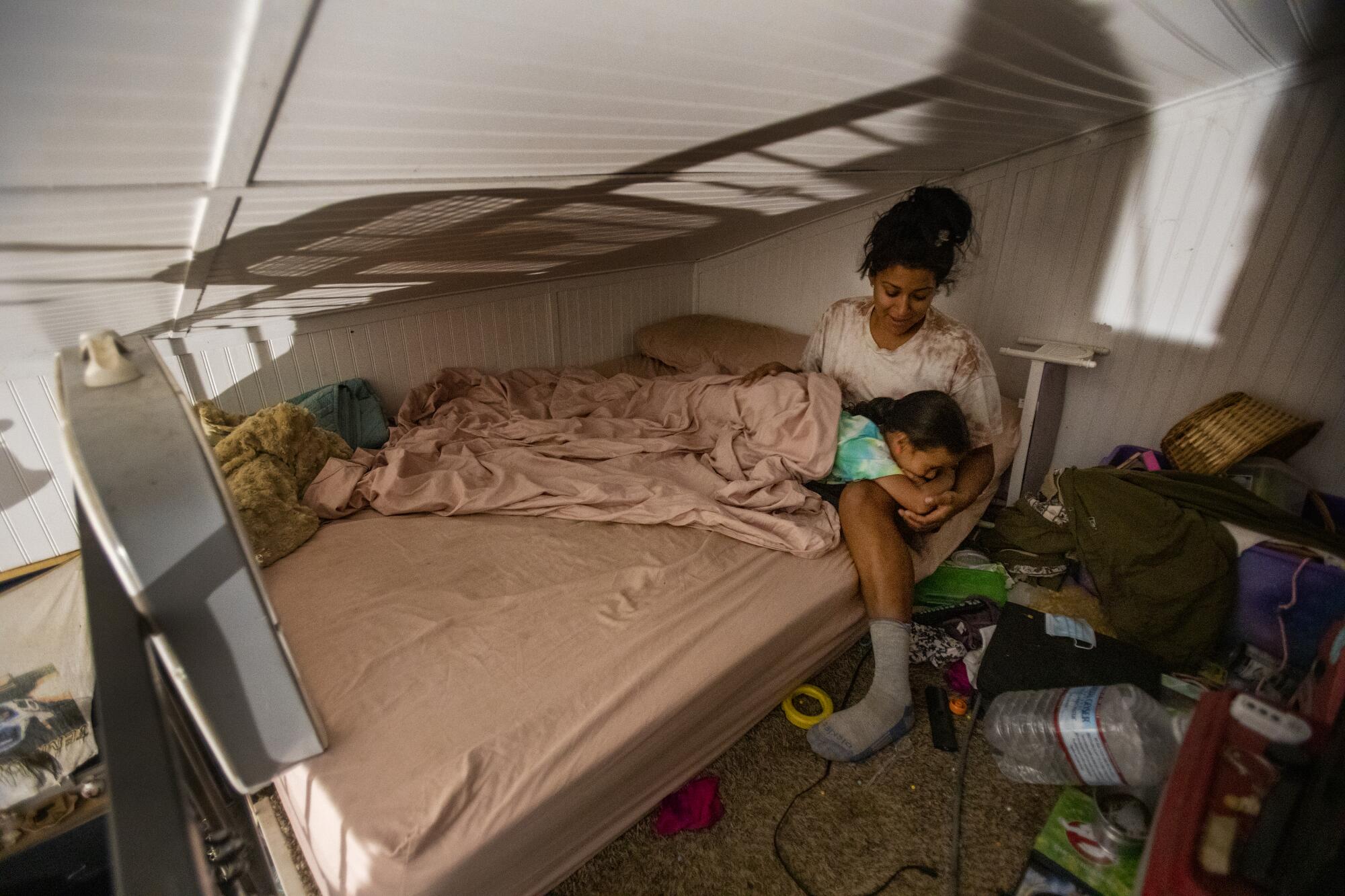 Inez Salinas sits on a bed beneath a low, slanting roof, holding River.