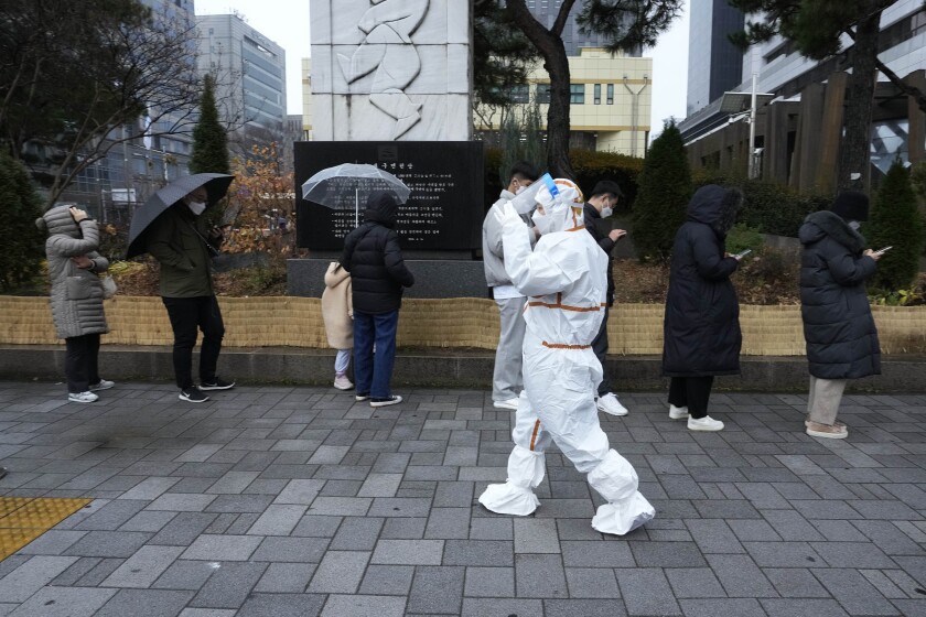 A medical workers passes by people as they wait for the coronavirus testing outside a public health center in Seoul, South Korea, Wednesday, Dec. 15, 2021. Halting its steps toward normalcy, South Korea will clamp down on social gatherings and cut the hours of some businesses to fight a record-breaking surge of the coronavirus that has led to a spike in hospitalizations and deaths. (AP Photo/Ahn Young-joon).