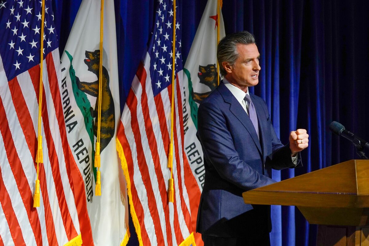 Gov. Gavin Newsom speaking at a lectern with the U.S. and California flags behind him.