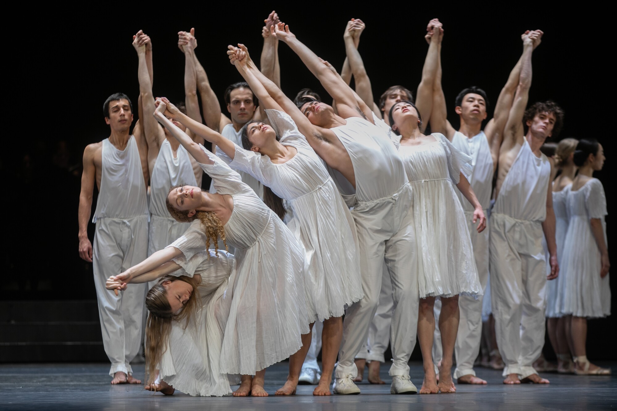 Dancers with raised arms and clasped hands form a rippling pattern.