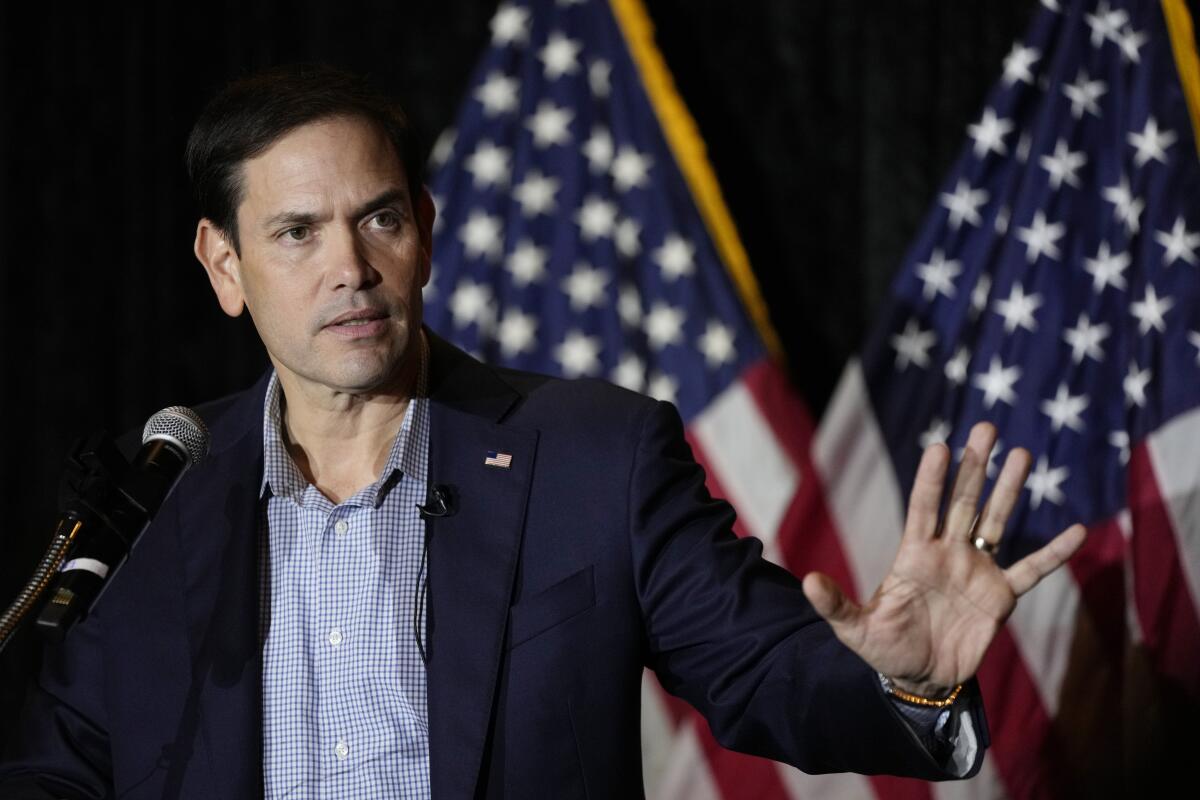 A man stands behind a lectern and gestures with his left hand.