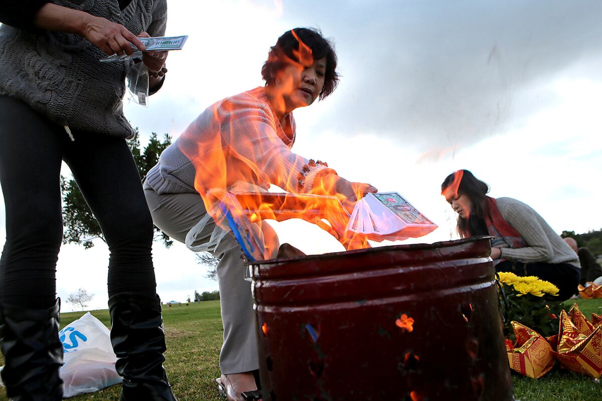 Deedee Xu burns a stack of fake money as she, her sister, Lili Xu, left, and daughter Jessica Wu honor a deceased relative at Rose Hills. Few cemeteries have bet as much on Chinese customers as the Whittier cemetery.