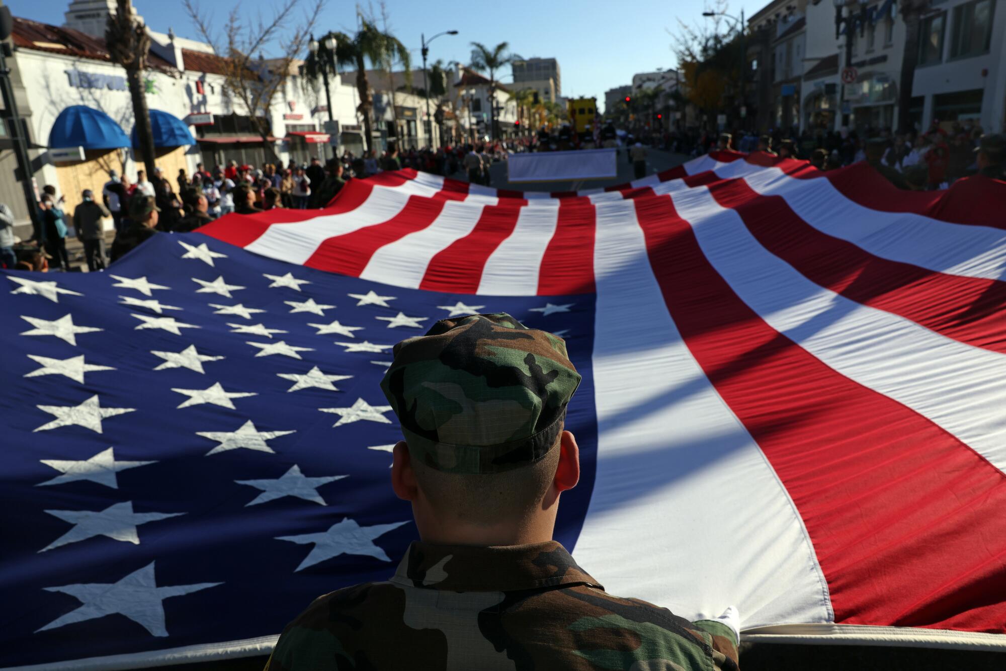 People in military fatigues carry a huge U.S. flag.