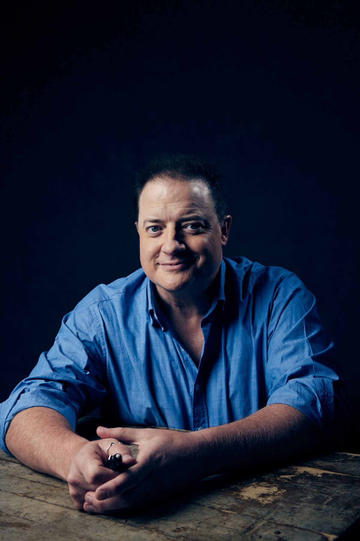 Brendan Fraser leans his arms on a table.