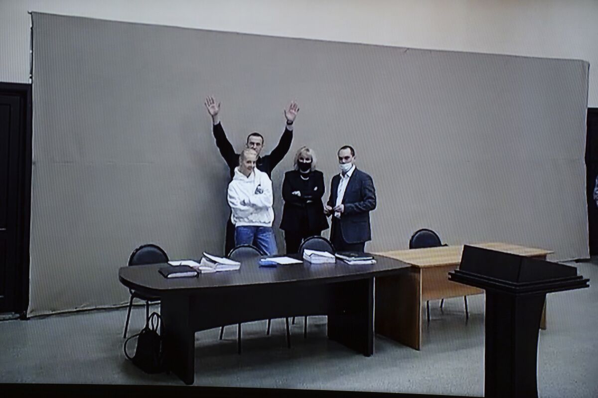 In this image provided by the Russian Federal Penitentiary Service, Russian opposition leader Alexei Navalny waves to journalists and supporters via a video link, as he stands next to his wife Yulia and his layers during a court session in Pokrov, Vladimir region, about 100 kilometers (62 miles) east of Moscow, Russia, Monday, Jan. 17, 2022. A new trial against Russian opposition leader Alexei Navalny has opened at the penal colony where he already is serving a prison term. Navalny is charged with fraud and contempt of court in the trial that opened on Tuesday. (AP Photo/Denis Kaminev)