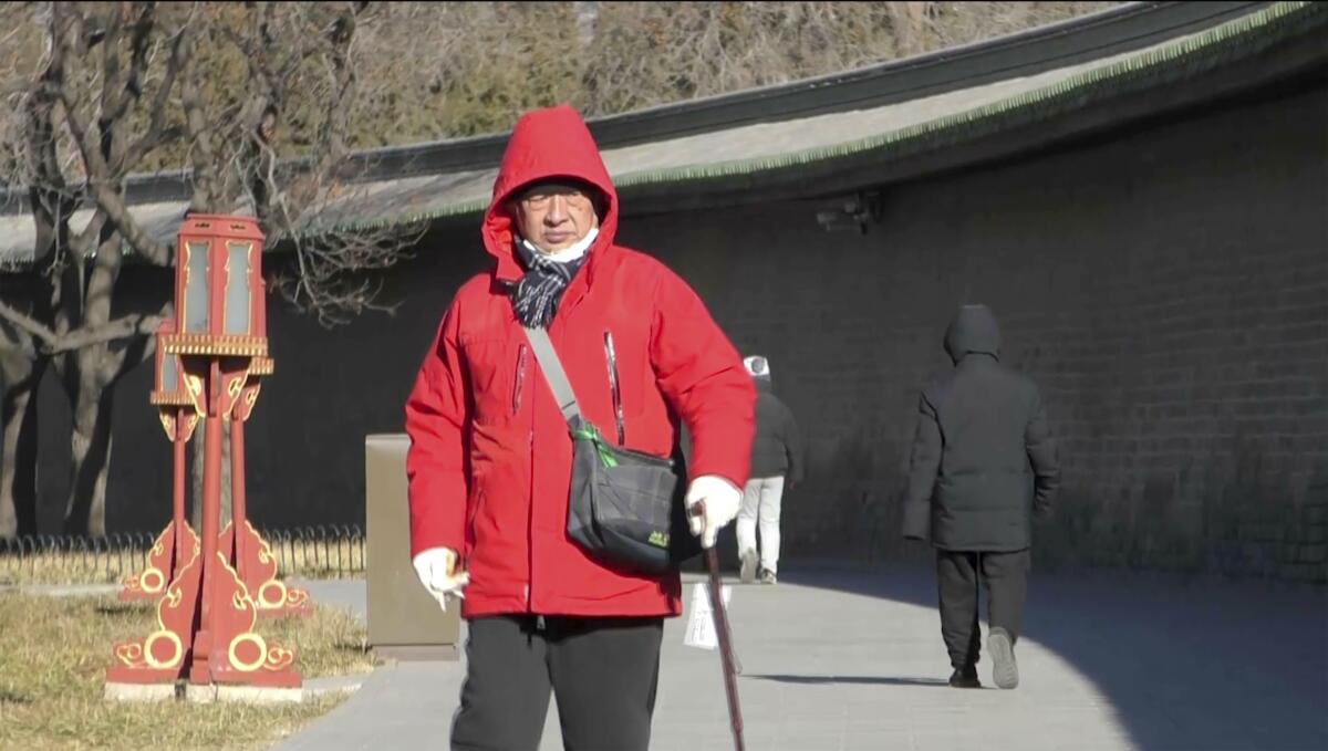 An older man in a coat pauses on a Beijing sidewalk.