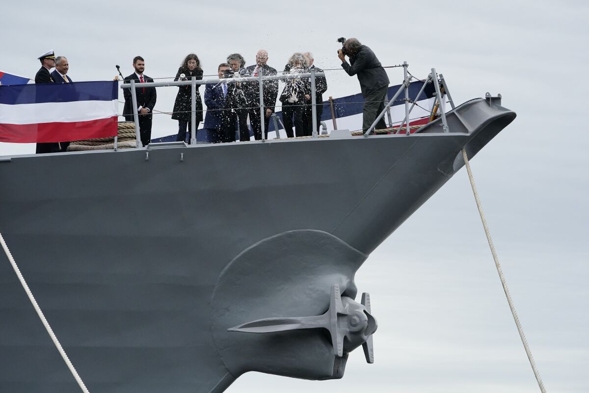 Erica Levin, left, Kate Levin Markel, center, and Laura Levin, the daughters of late Sen. Carl M. Levin, D-Michigan, smash champagne bottles to christen a warship named for the senator, Saturday, Oct. 2, 2021, at Bath Iron Works in Bath, Maine. The ship is an Arleigh Burke class destroyer.(AP Photo/Robert F. Bukaty)