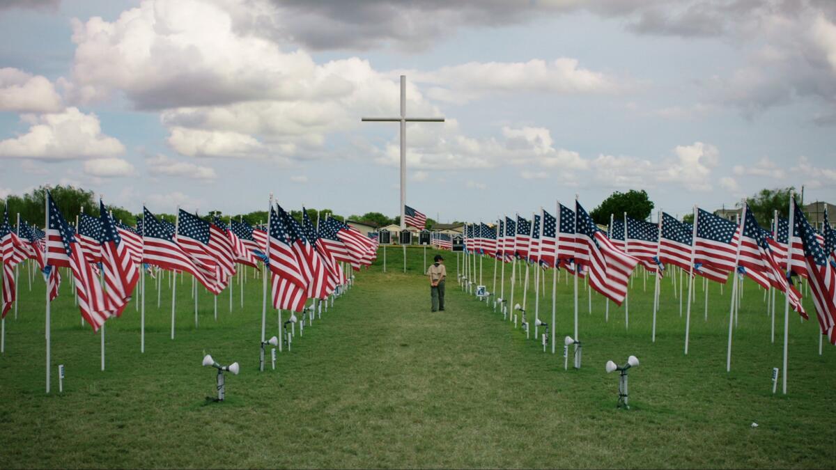 A boy stands among rows of flags and a giant cross in the background.