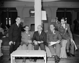 Several men in business suits sit on a couch in an ornate room.