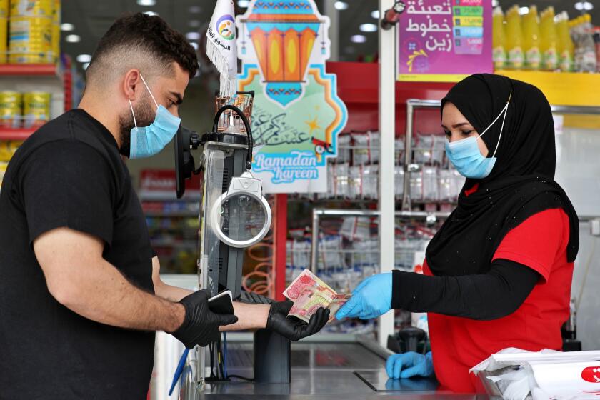 In this Saturday, May, 2, 2020, photo, a man uses banknotes to pay for his purchases at the mall in Basra, Iraq. The coronavirus pandemic has reawakened debate about the continued viability of what has been the physical lifeblood of global economies: paper money and coins. (AP Photo/Nabil al-Jurani)