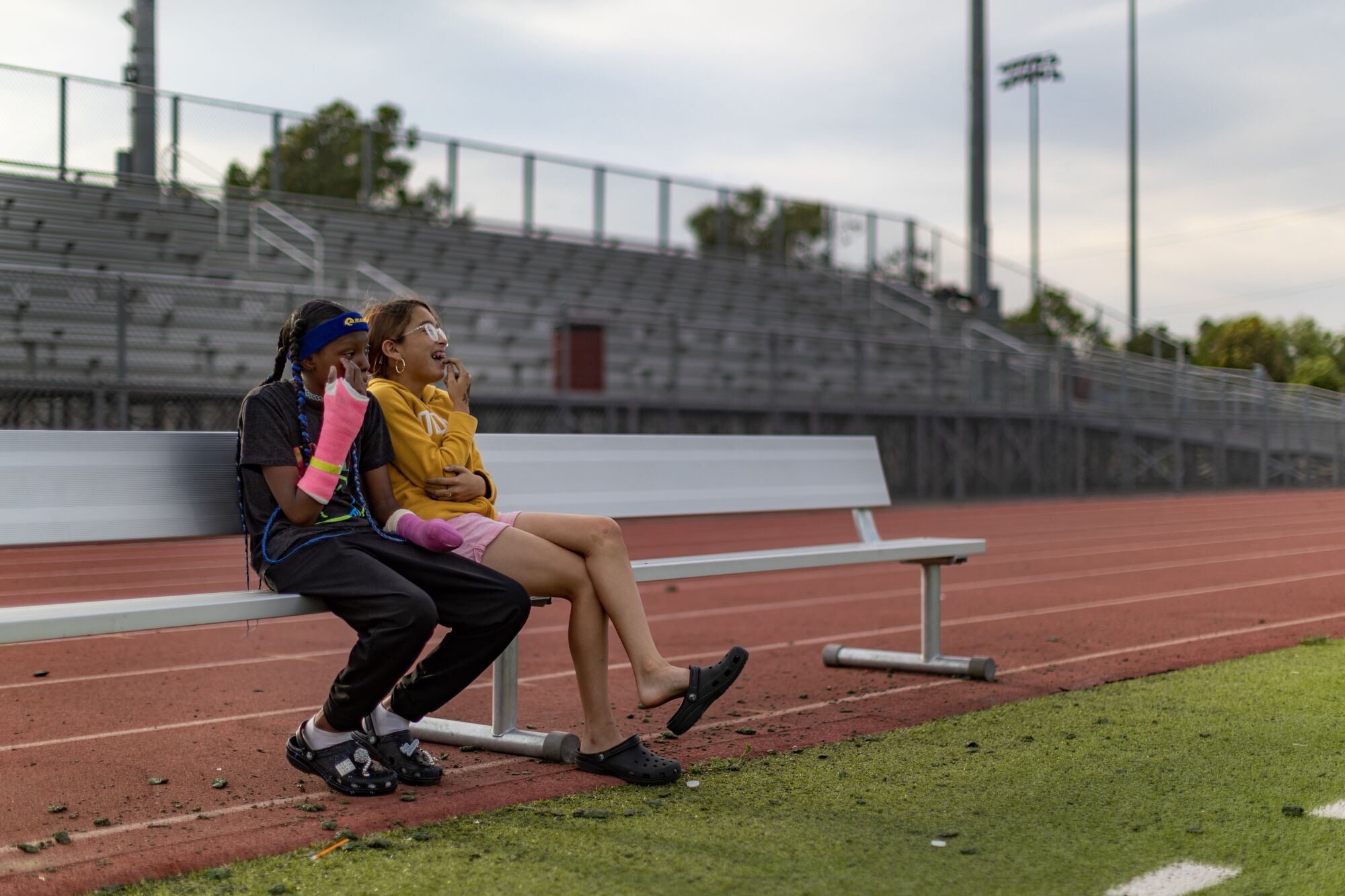 With both arms fitted with casts, La'Veyah Mosley, 12, left, sits with a friend to watch her twin sister La'Viyah practice