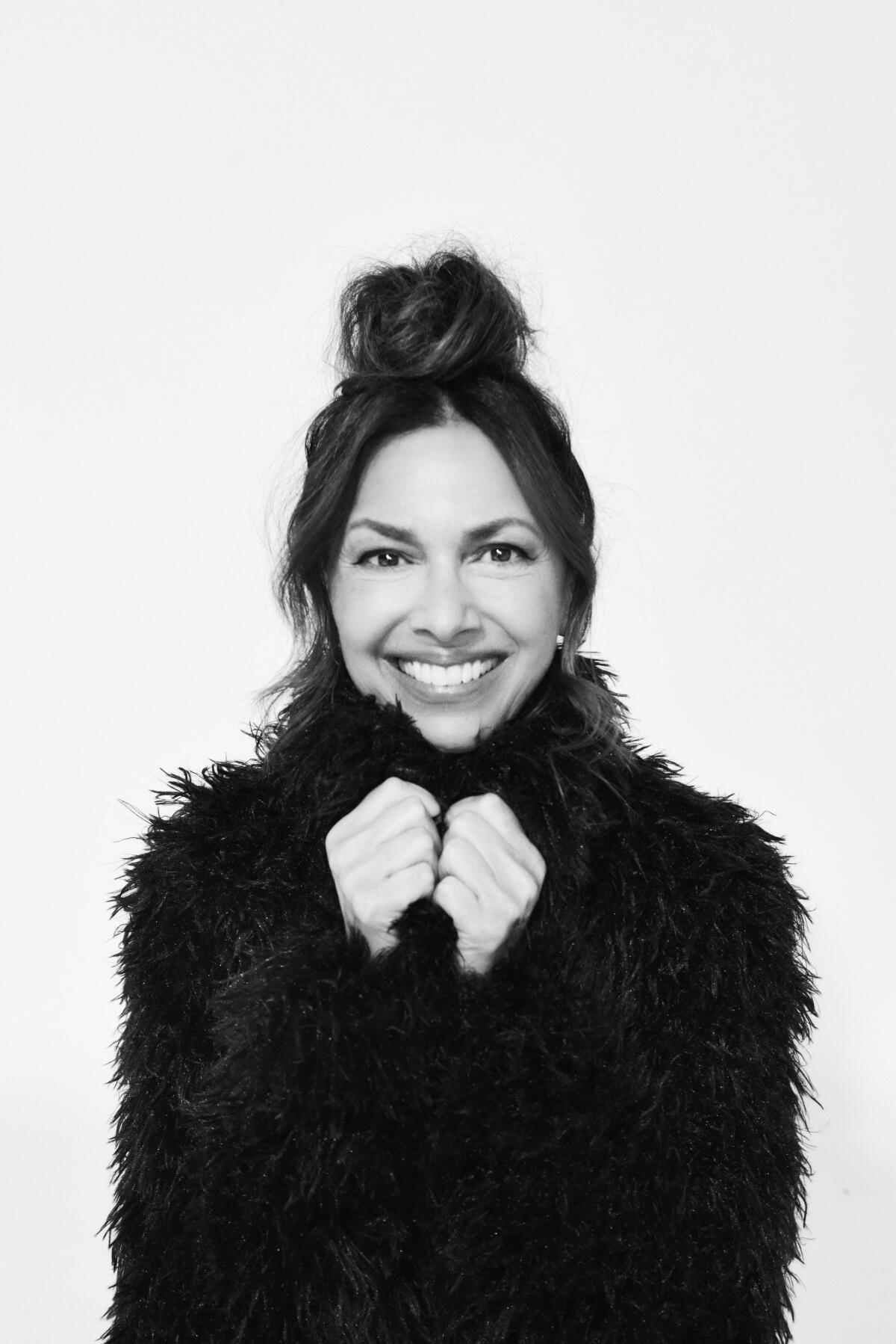 Susanna Hoffs, lead singer of the Bangles, smiles while holding her black furry coat closed.