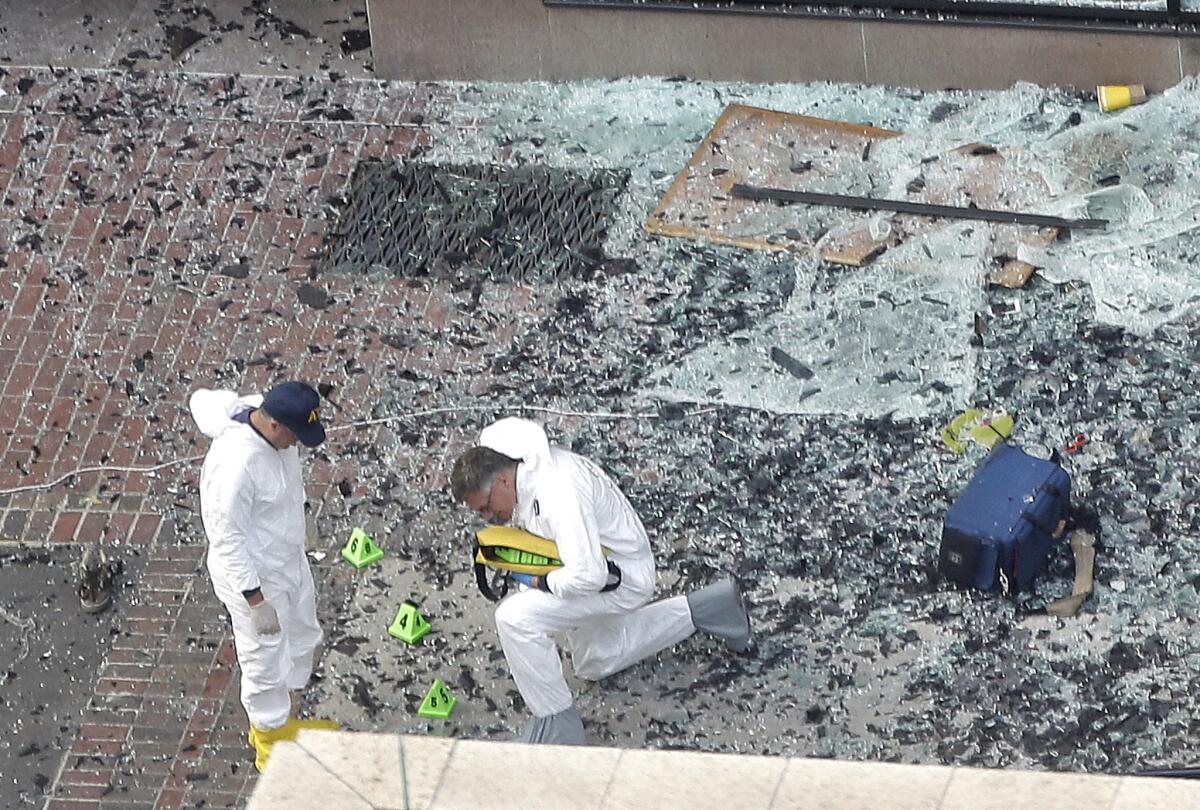 Two men in hazardous materials suits put numbers on the shattered glass and debris as they investigate the scene at the first bombing on Boylston Street in Boston.