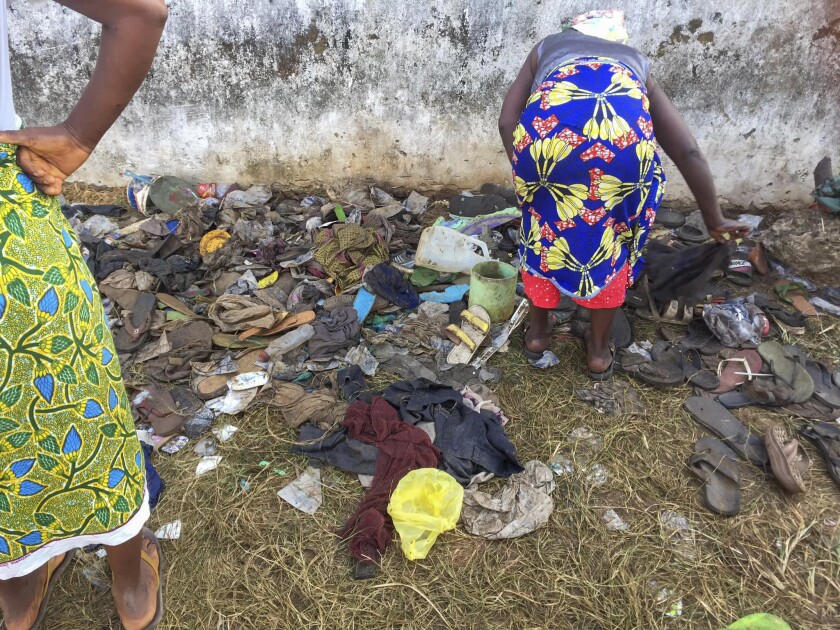 This photograph provided by Augustine D Wallace shows a woman searching through shoes Thursday Jan. 20, 2022 at the entrance of a field where 29 persons, including 11 children and a pregnant woman have been confirmed killed after they were trampled upon in a stampede at a Christian crusade in New Kru Town, outside Monrovia, Liberia, Wednesday night. The stampede erupted when a group of gangsters, some carrying knives moved on the crusade ground and attacked worshipers. (Augustine D Wallace via AP)