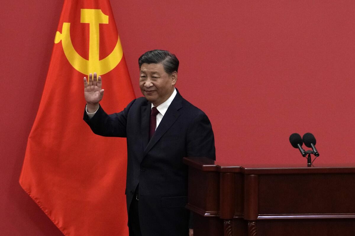 President Xi Jinping waves and stands next to a Chinese flag