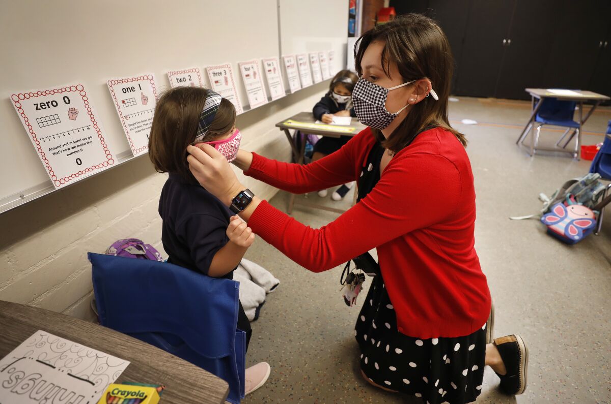 Teacher Heather Hernandez helps a student with her mask