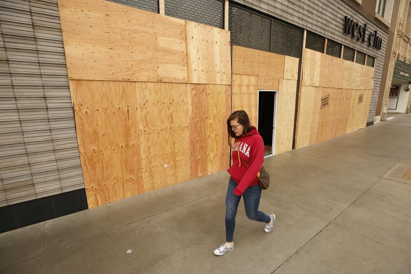 BEVERLY HILLS, CA - APRIL 02, 2020 Elena Girotto walks past the West Elm store which features modern furniture on Colorado Blvd in Pasadena Thursday morning April 02, 2020 which is boarded up as some businesses in Pasadena and Beverly Hills have boarded up the front of their stores during the coronavirus Covid-19 pandemic possibly to avoid vandalism during the crisis. Elena lives nearby and is walking to her job where she is the legal administrator at a law firm but her hours have been cut from 50 hours a week to 5 hours a week. (Al Seib / Los Angeles Times)