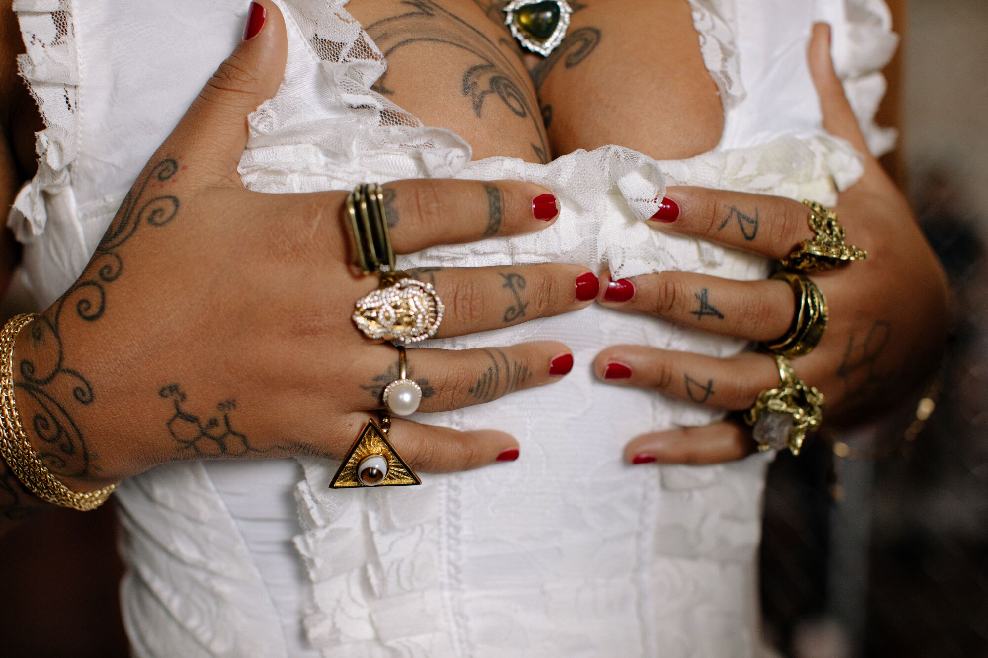 Close-up of a woman's bust. The woman is wearing a white dress and has tattoos on her hands and fingers.