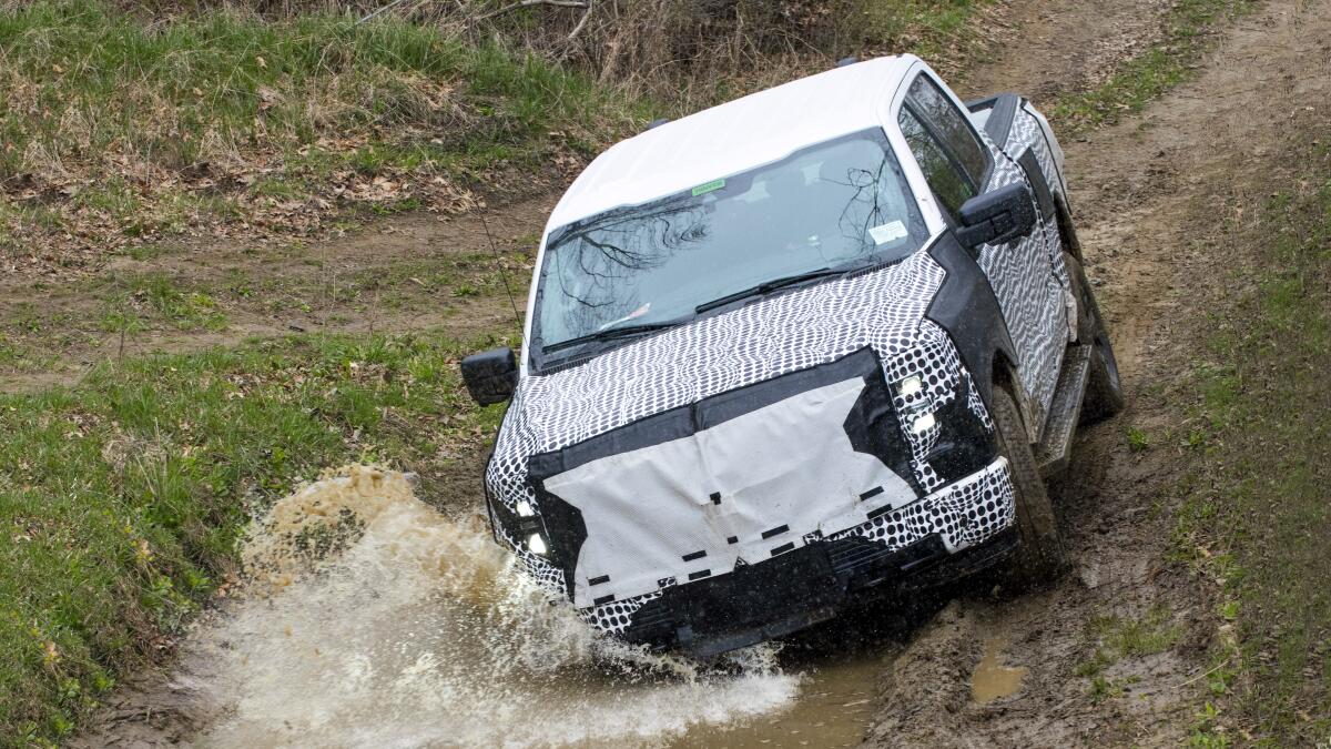 Ford put the Lightning through rigorous off-road tests. Here a truck hits a puddle of water on a dirt road in a forest.