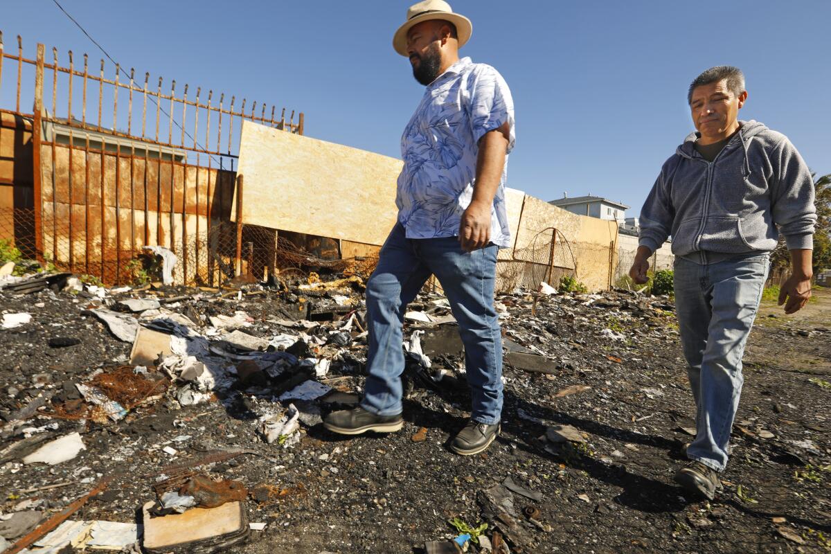 Germán Magaña, left, and Gustavo Flores Álvarez walk past the remains of a homeless encampment fire.