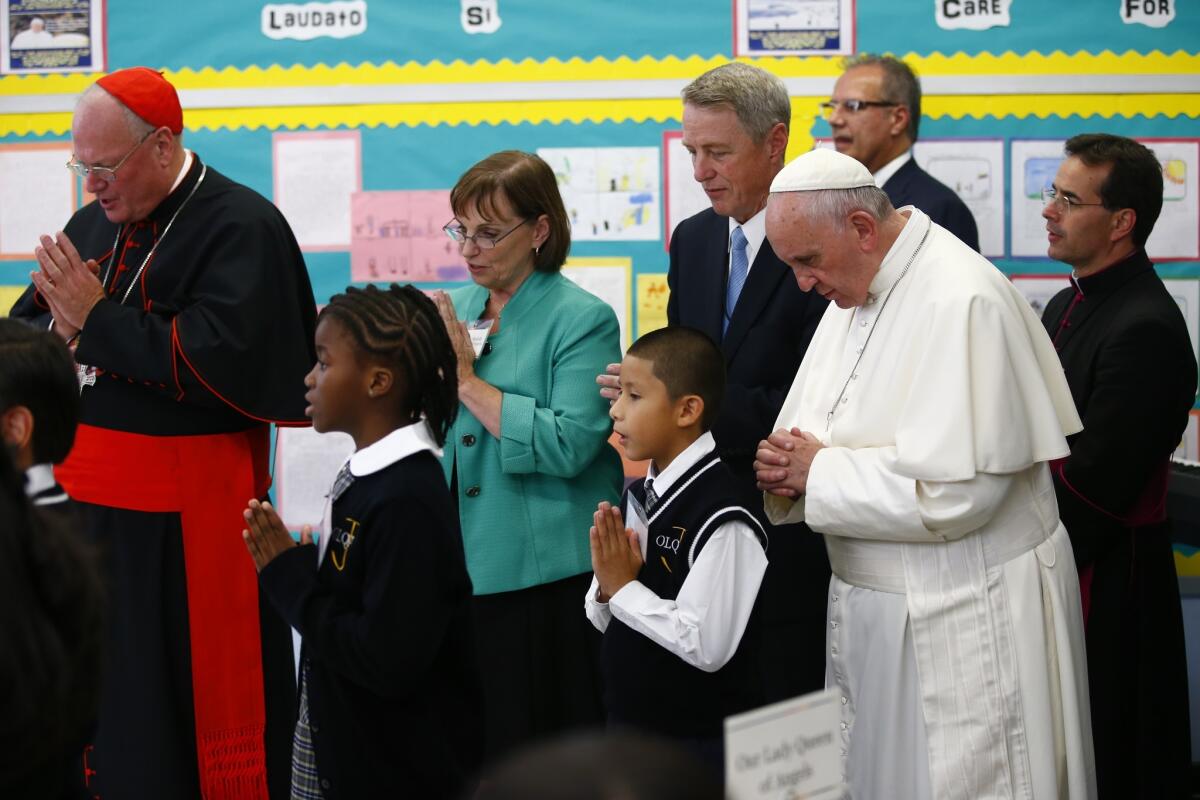 Pope Francis, accompanied by Cardinal Timothy Dolan, left, and Joanne Walsh, principal of Our Lady Queen of Angels School, prays as he visits the school in East Harlem on Friday.