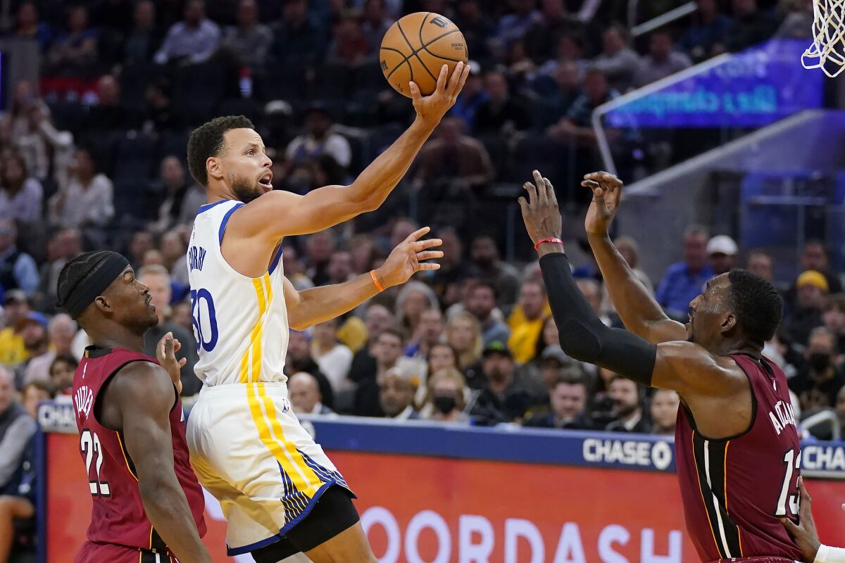 Stephen Curry, base de los Warriors de Golden State, dispara entre Jimmy Butler y Bam Adebayo, del Heat de Miami, el jueves 27 de octubre de 2022 (AP Foto/Jeff Chiu)